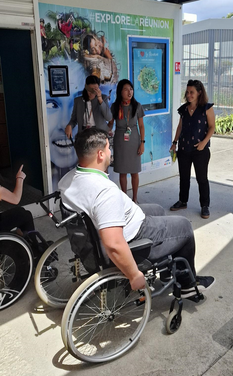 Réhane (FRT) sur un fauteuil roulant devant le bureau d'information touristique de Roland Garros avec le reste de l'équipe et Camille (La Réunion pour Tous)