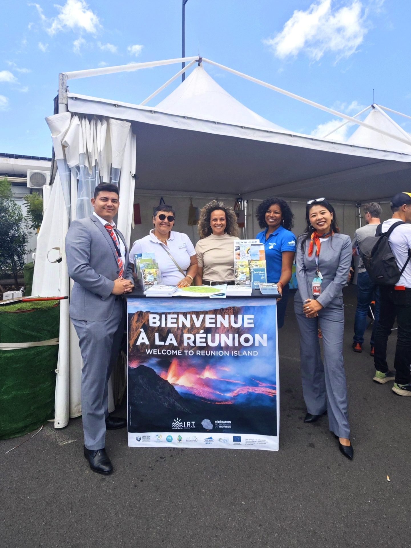 Mathieu (FRT), Martine (Côté Est), Dephine (FRT), Sabrina (FRT), et Li (FRT) posent devant le stand d'accueil de La Réunion pour les coureurs et leurs proches à l'aéroport de Roland Garros.