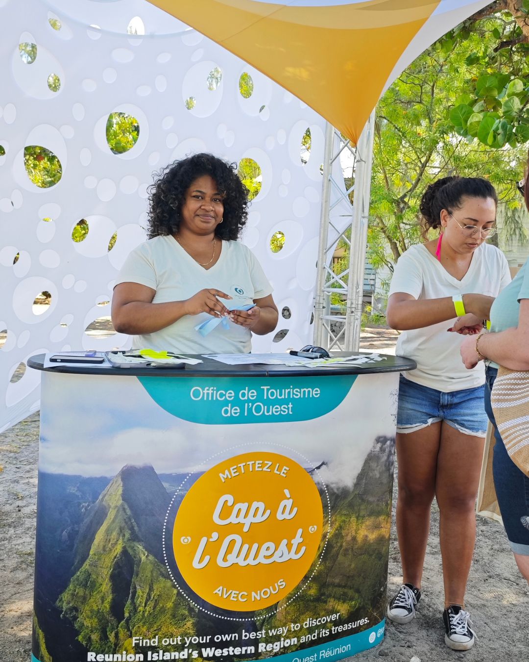 Une des collaboratrices de l'office de tourisme de l'ouest qui pose devant un comptoir de l'office où il est inscrit "cap à l'ouest"