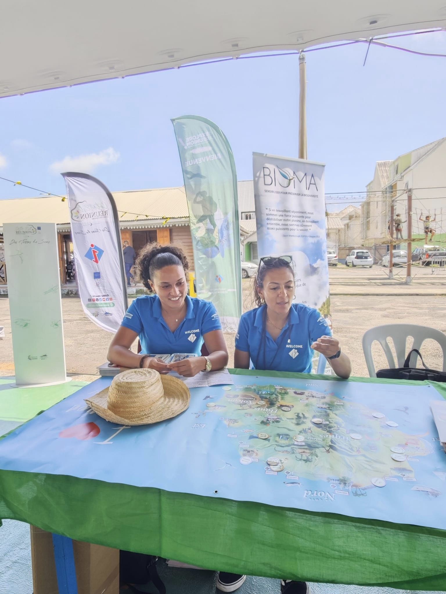 Heloise et Elodie (FRT) assises devant une carte de La Réunion, prêtes pour faire jouer les visiteurs en leur faisant placer des lieux touristiques sur la carte